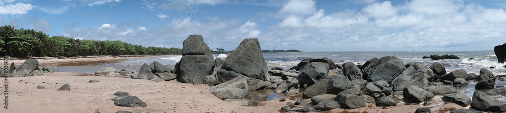 Panoramic image of black dark boulders lying on a beach along the coast of Axim Ghana West Africa