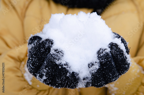Women's hands in black gloves hold a lot of snow. Taken in close-up