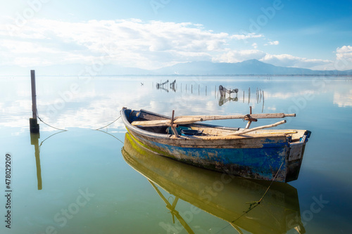 Close up of a small fishing boat. Reflection on the sea water of a small boat. Flat and calm sea reflecting the sky.