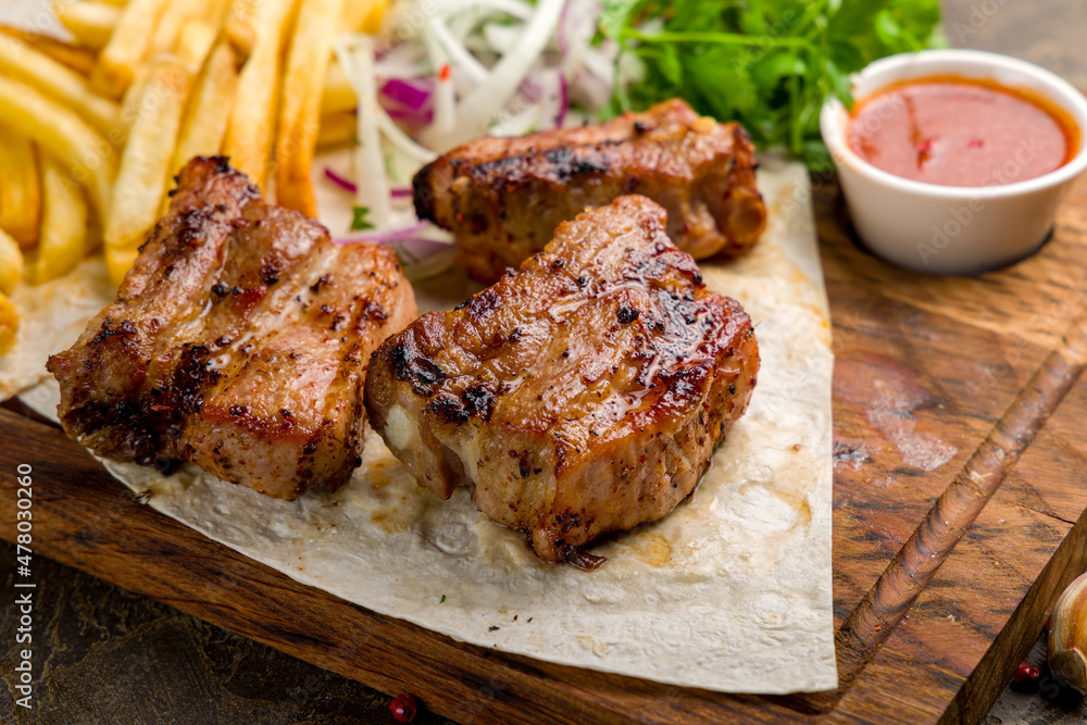 skewers of pork ribs with french fries, red onion and tomato sauce on the board close up