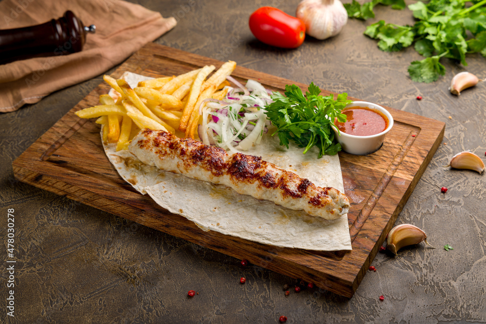Lula kebab chicken with french fries, red onion and tomato sauce on the board