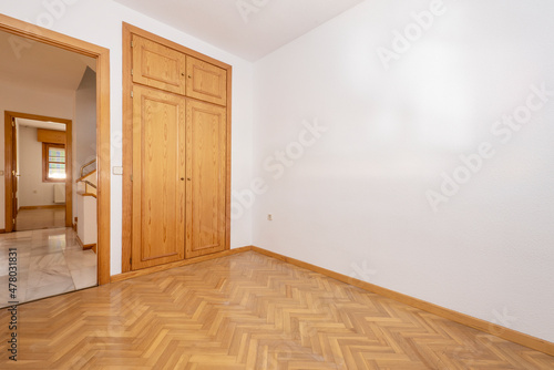Empty room with built-in pine wood wardrobe and oak parquet floors