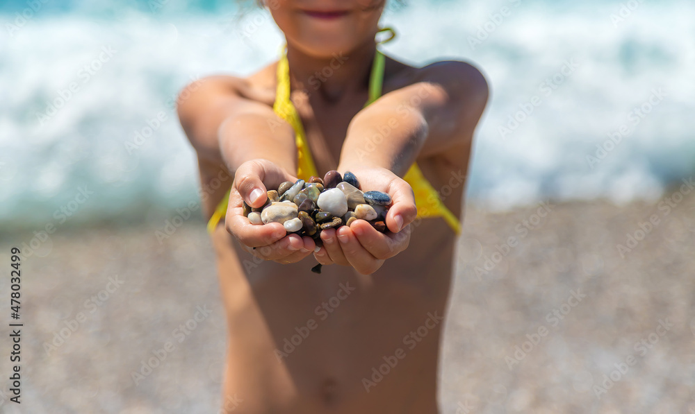A child on the beach holds sea stones in her hands. Selective focus.