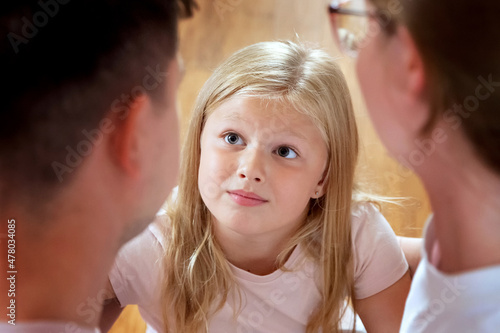 A little blonde girl looks questioningly at her parents. Close-up. Top view. The child is interested, children's questions are a concept.