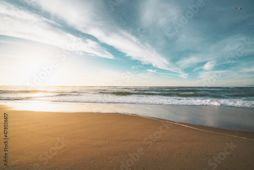 Sunset on the beach. Beautiful tranquil scene of empty sand beach, turquoise colored water, and cloudy sky