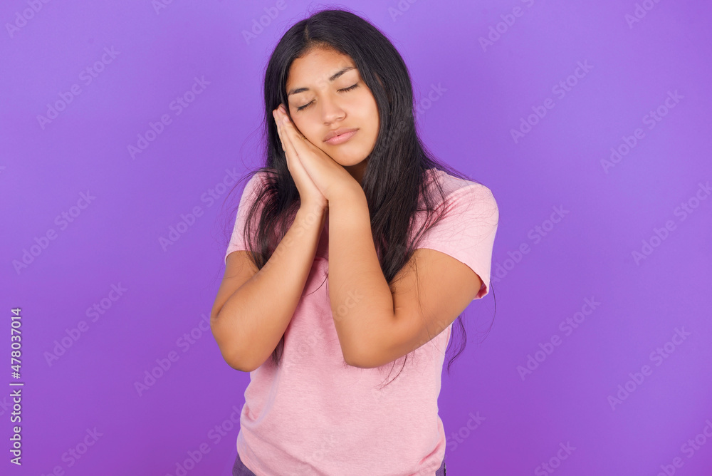 Hispanic brunette girl wearing pink t-shirt over purple background sleeping tired dreaming and posing with hands together while smiling with closed eyes. Hispanic brunette girl wearing pink t-shirt over purple background sleeping tired dreaming and posing with hands together while smiling with closed eyes.