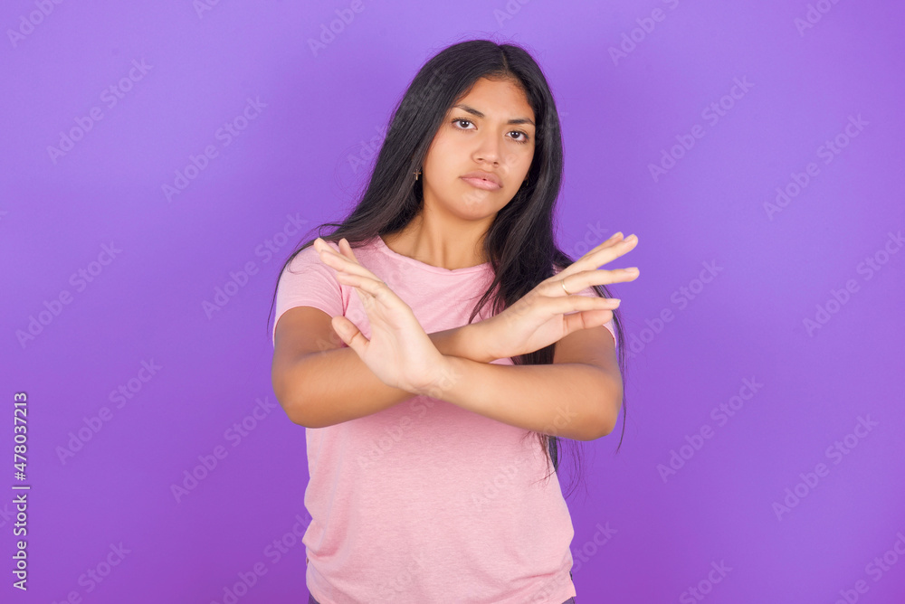 Hispanic brunette girl wearing pink t-shirt over purple background Rejection expression crossing arms doing negative sign, angry face Hispanic brunette girl wearing pink t-shirt over purple background Rejection expression crossing arms doing negative sign, angry face