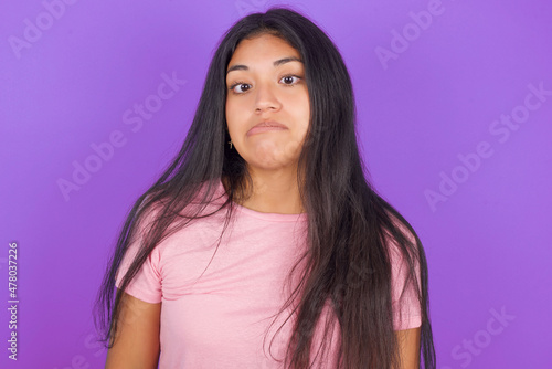Hispanic brunette girl wearing pink t-shirt over purple background making grimace and crazy face, screaming out of control, funny lunatic expressing freedom and wild.