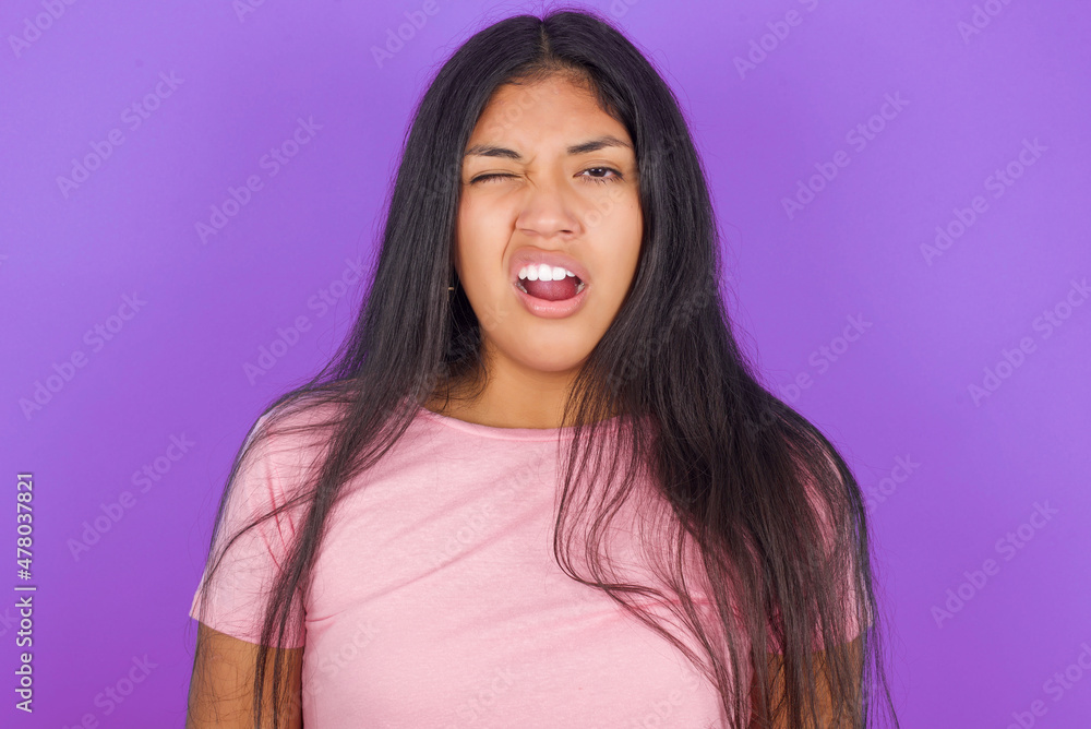 Hispanic brunette girl wearing pink t-shirt over purple background yawns with opened mouth stands. Daily morning routine Hispanic brunette girl wearing pink t-shirt over purple background yawns with opened mouth stands. Daily morning routine