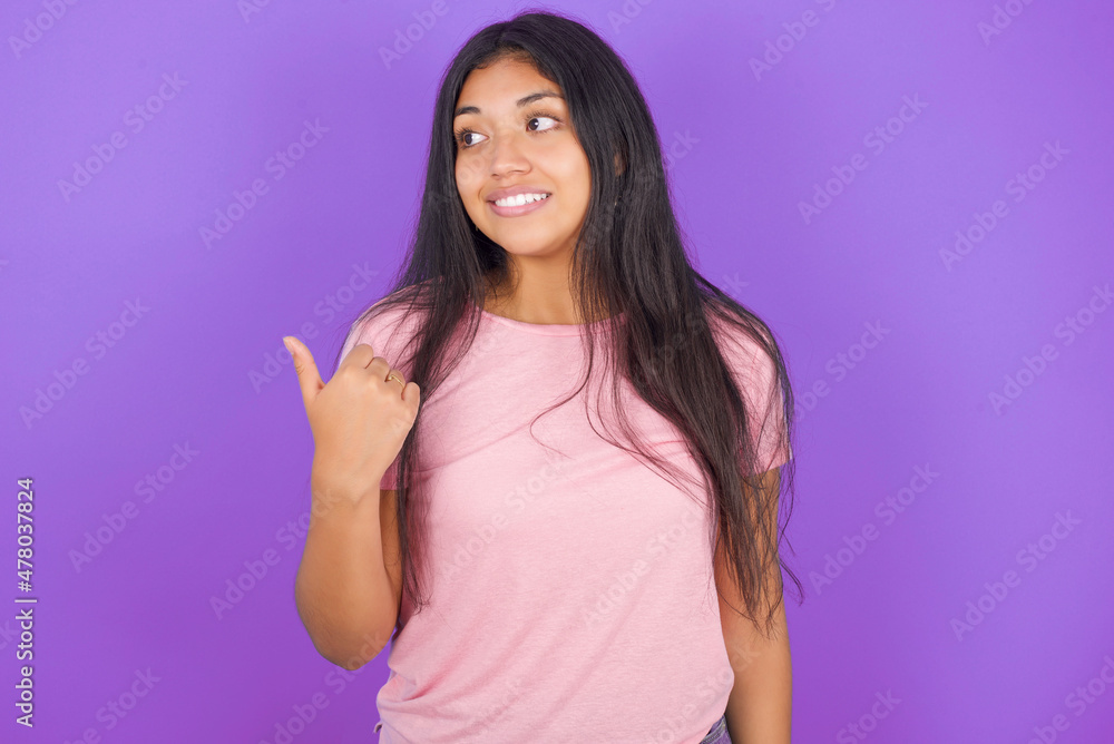 Obraz premium Hispanic brunette girl wearing pink t-shirt over purple background points away and gives advice demonstrates advertisement