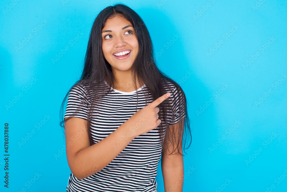 hispanic girl wearing striped t-shirt standing over blue background glad cheery demonstrating copy space look novelty hispanic girl wearing striped t-shirt standing over blue background glad cheery demonstrating copy space look novelty