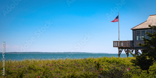 Seascape over Martha's Vineyard in summer with the view of waving American flag and beach house in partial view. Tranquil coastal landscape on Cape Cod.