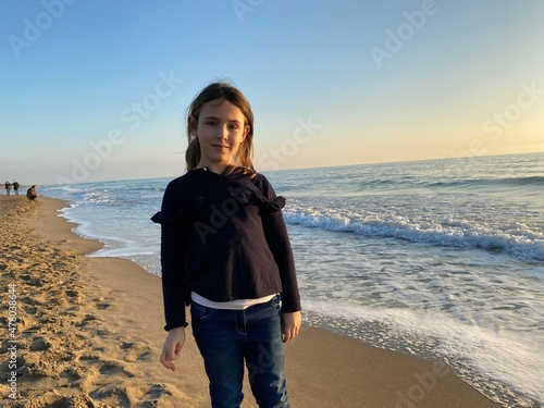 Young girl looking at the camers, walking on the beach, winter sea, sunset photo