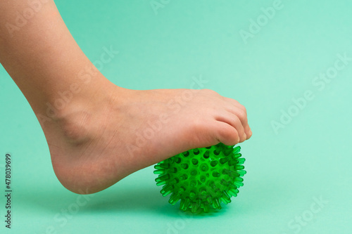 green needle ball for massage and physical therapy on a green background with a child's foot, the concept of prevention and treatment of foot valgus