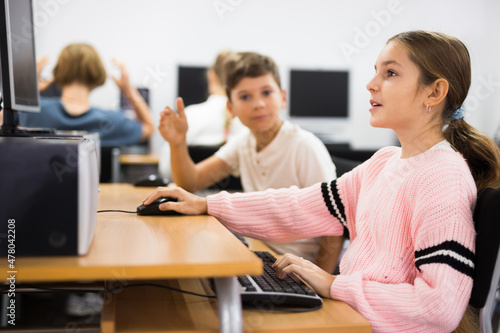 Pre-adolescent children learn to work at a computer in a school classroom