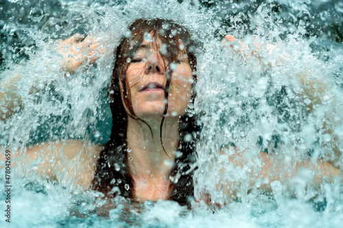 beautiful young cute sexy redhead woman under the splashing falling water shower waterfall in the Spa Wellness pool