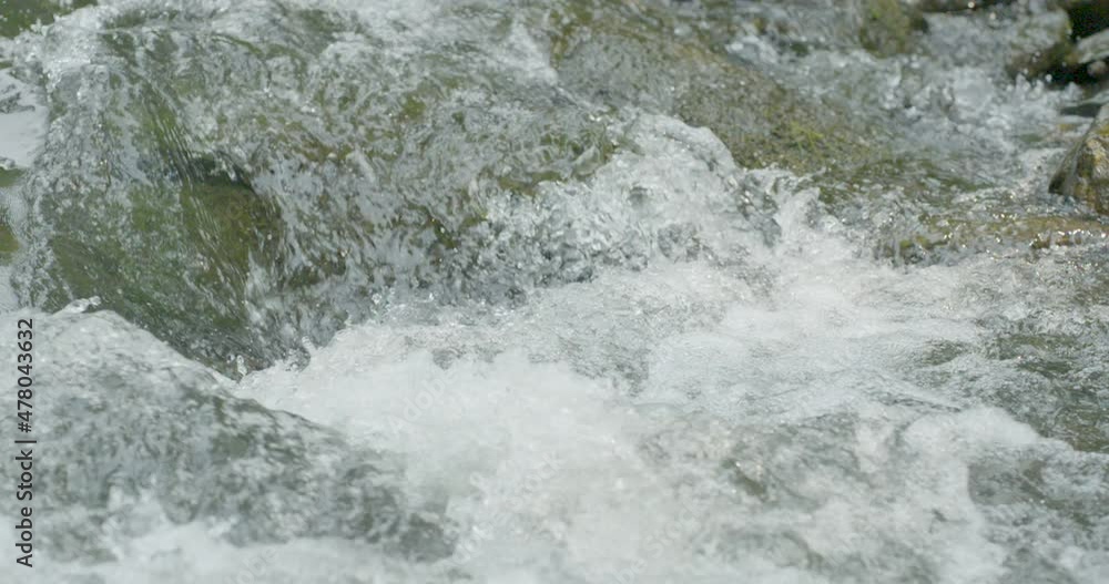 Slow motion close up of quickly flowing fresh water rapids as it crashes over river stones and rocks showing details of bubbles and splashing as the spring flows downstream Slow motion close up of quickly flowing fresh water rapids as it crashes over river stones and rocks showing details of bubbles and splashing as the spring flows downstream