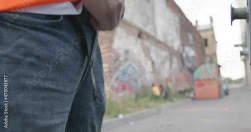 Vandal zips up the fly on jeans after peeing on the street in broad daylight, forgetting to fasten leather belt, then put his hands in pockets as if nothing had happened, close up. photo