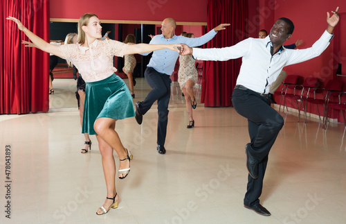 Portrait of young positive people dancing twist in pairs at dance hall