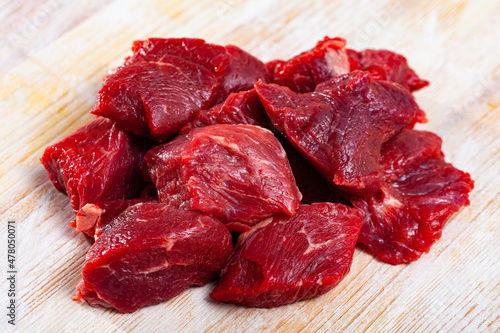 Chopped juicy raw beef meat on wooden surface. Main ingredient for stew cooking ..