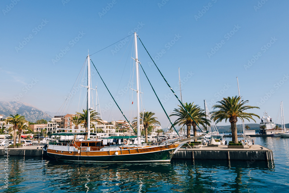 Sailing yacht stands at the pier lined with palm trees in the resort of Porto. Montenegro