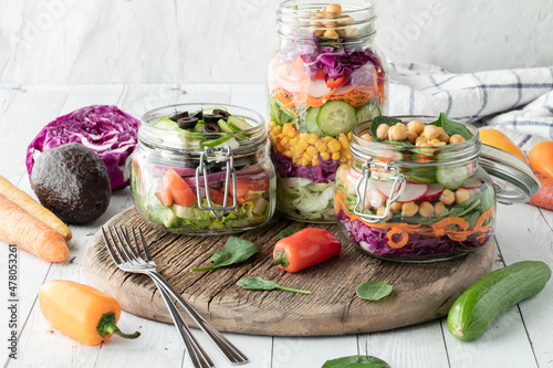 Salad jars on a rustic wooden board, with fresh ingredients all around. 