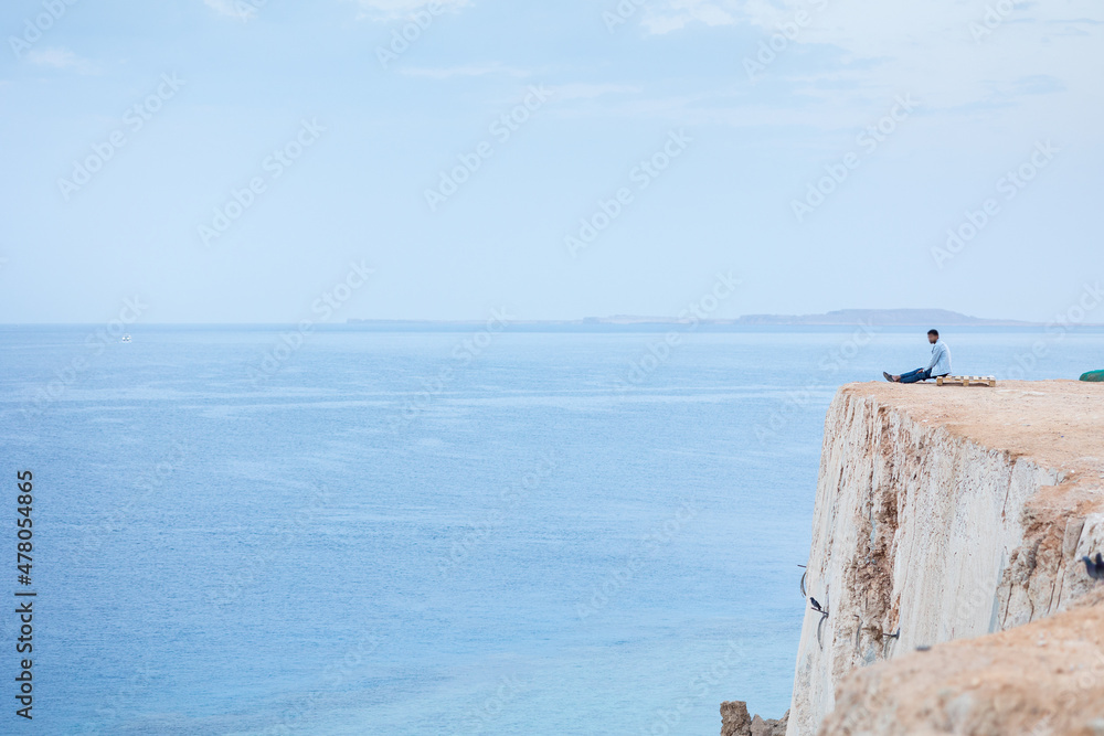 Man greets sunrise of sun on high mountain above sea. Aerial view to calm blue sea with rocky coastline. Panoramic view of dawn above horizont in summer morning, Sharm El Sheikh, Egypt. Man greets sunrise of sun on high mountain above sea. Aerial view to calm blue sea with rocky coastline. Panoramic view of dawn above horizont in summer morning, Sharm El Sheikh, Egypt.