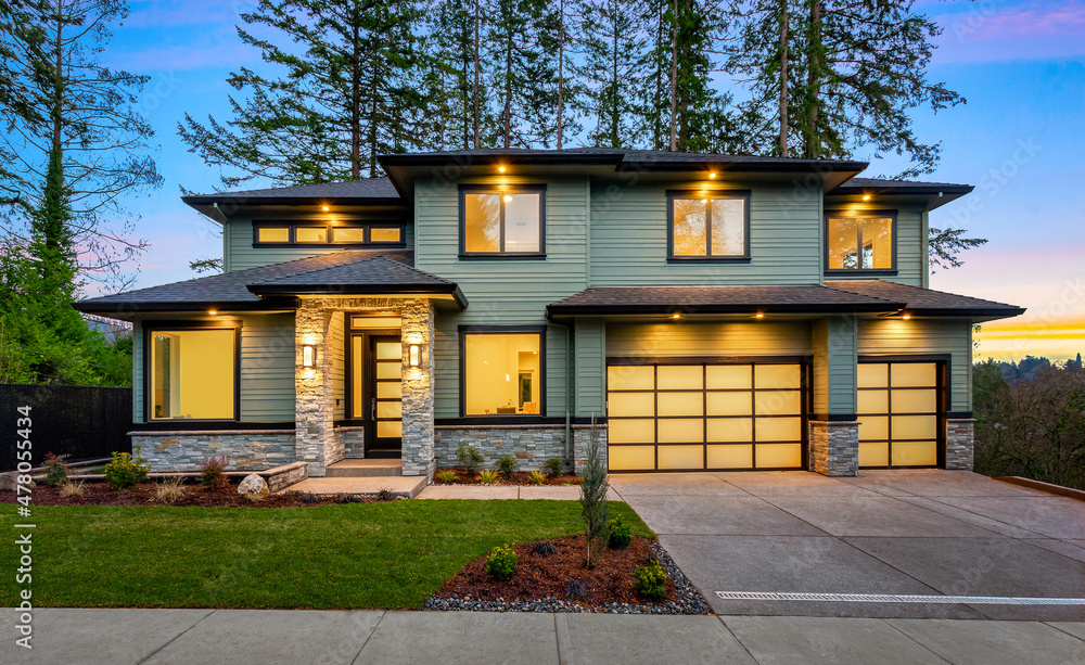 Beautiful modern luxury home exterior at sunset. Features three car garage, two stories, stone Beautiful modern luxury home exterior at sunset. Features three car garage, two stories, stone