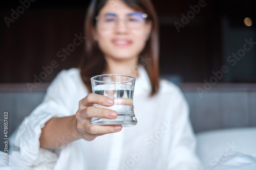 Happy woman holding water glass, female drinking pure water on bed at home. Healthy, Refreshment, lifestyle concept