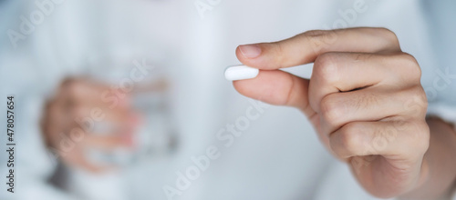 Photo Adult woman holding pill and glass of water, female taking medicine on bed at home