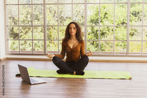 Free Download Healthy beautiful Young hispanic womanWearing sexy clothes showing breasts practice yoga practice teaching techniques on laptop calm mind meditation Sit on yoga mat in glass room at home - GFXLoad