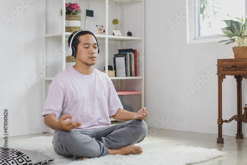 Handsome young asian man wearing wireless headphone meditation at home