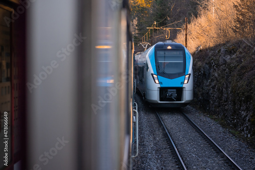 Modern blue and white passenger train coming towards another train on adjacent track. Two trains meeting on a parallel tracks.