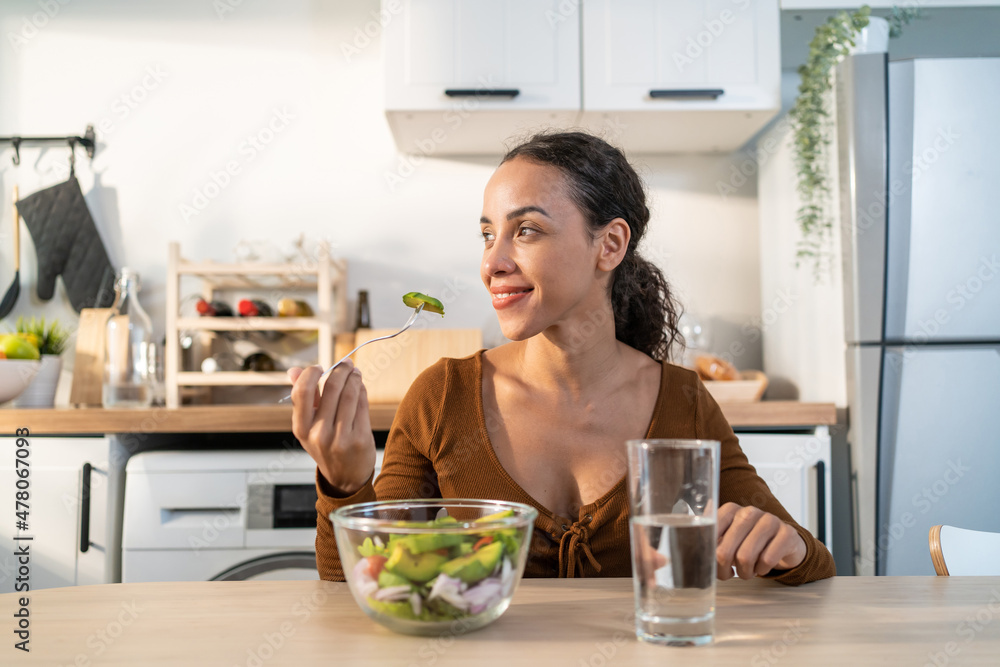 Latino attractive woman wear apron eat green salad in kitchen at home. Latino attractive woman wear apron eat green salad in kitchen at home.