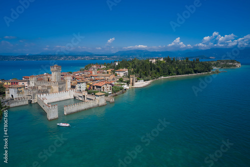 Boat with tourists near the main castle. Aerial view on Sirmione sul Garda. Italy, Lombardy. Rocca Scaligera Castle in Sirmione. View by Drone.