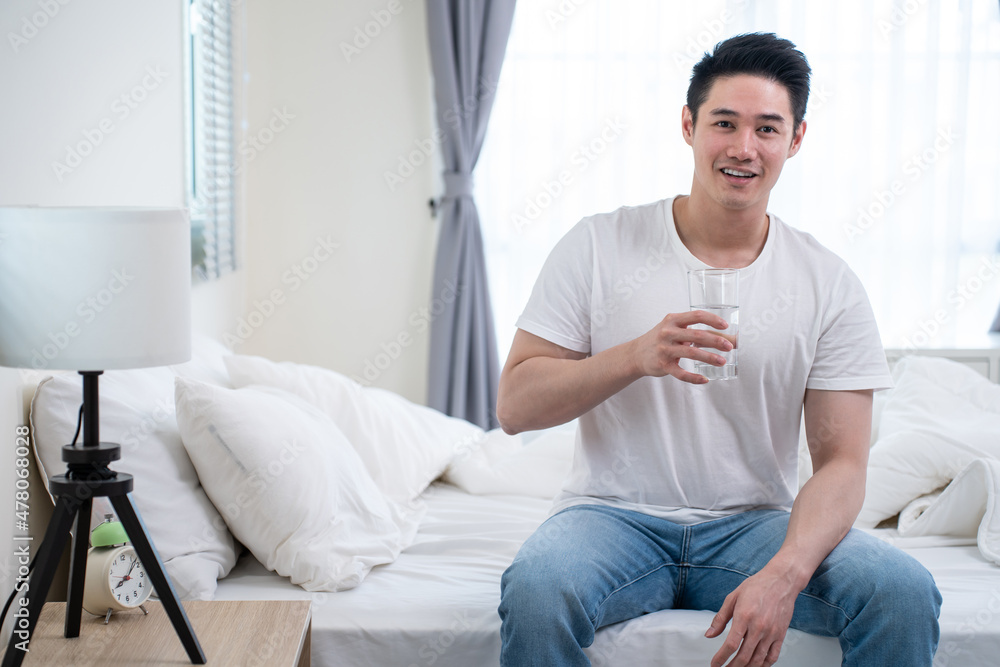 Portrait of Asian active strong man holding clean water in bedroom.