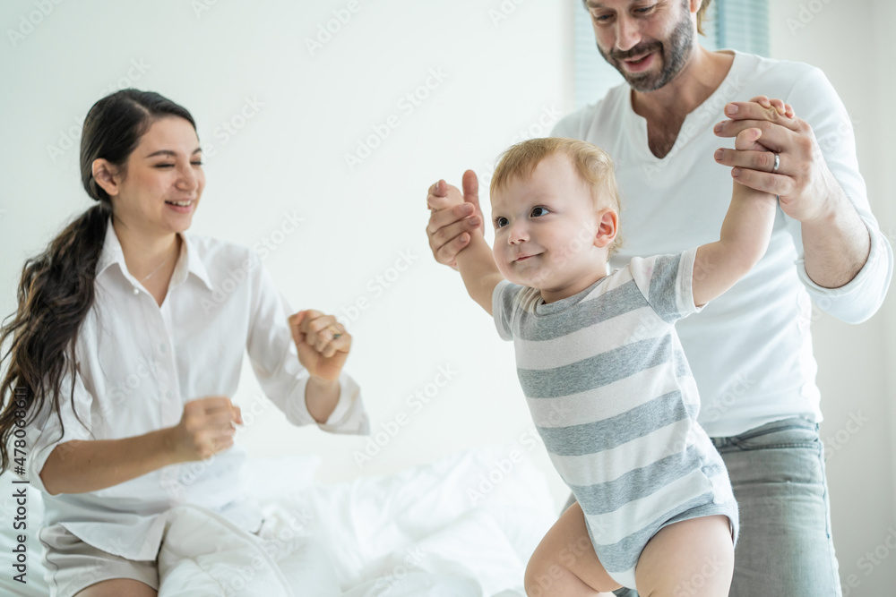 Caucasian loving parents play with baby boy child on bed in bedroom. Caucasian loving parents play with baby boy child on bed in bedroom.