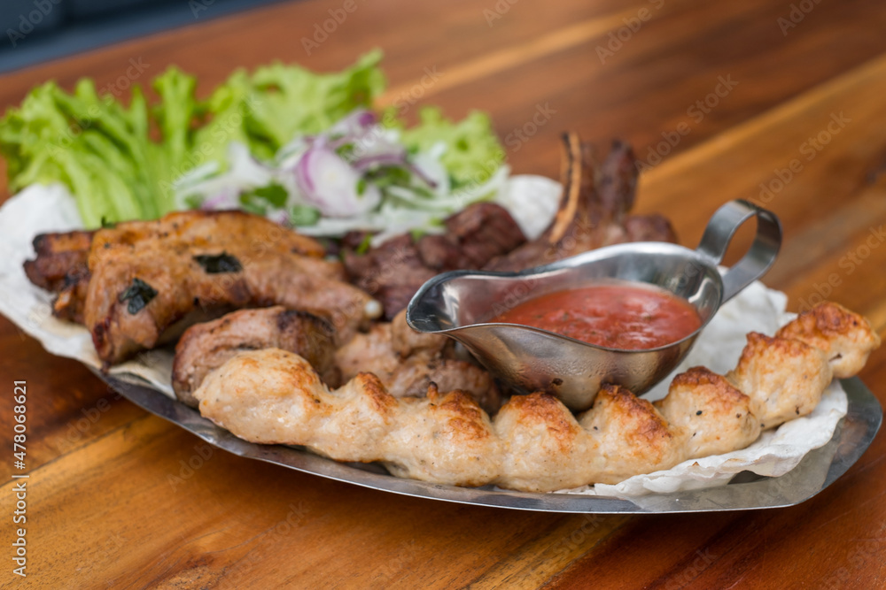 Assorted delicious grilled meat with lettuce and onion. Mixed grilled bbq meat with tomato sauce.Lamb, chicken. Top view, close up with copy space. Assorted delicious grilled meat with lettuce and onion. Mixed grilled bbq meat with tomato sauce.Lamb, chicken. Top view, close up with copy space.