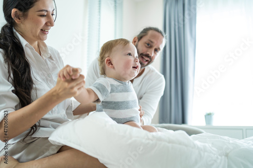 Caucasian loving parents play with baby boy child on bed in bedroom. 