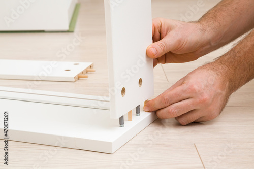 Fotografia Young adult man hands assembling white wooden boards of furniture for living room, kitchen or other places
