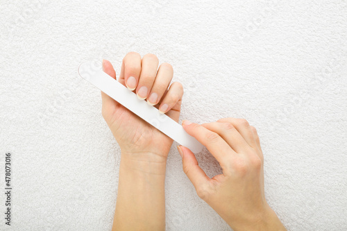 Young adult woman hand using nail file and filing nails on white towel background. Closeup. Point of view shot. Care about fingernails. Top down view.