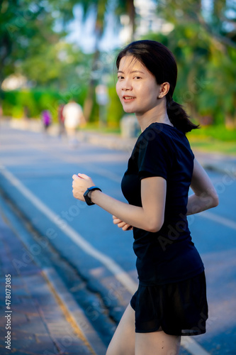 Asian woman wearing a black dress jogging in the park near river in the city