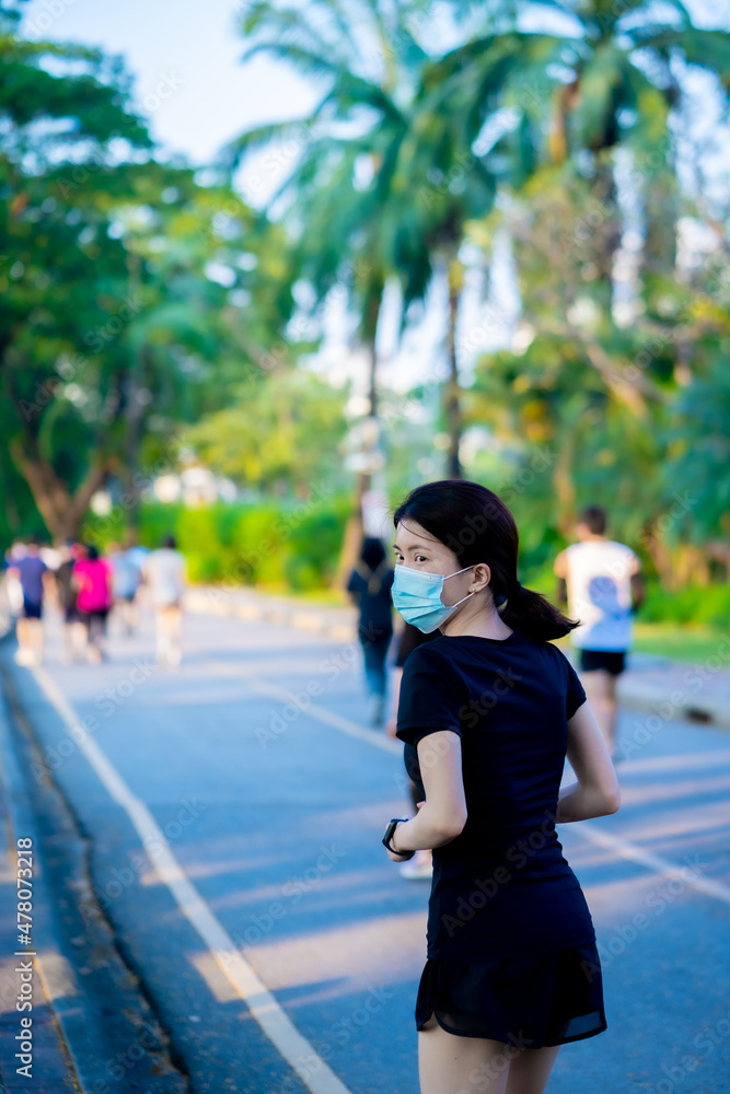Asian woman wearing a black dress  wearing medical mask jogging in the park near river in the city 