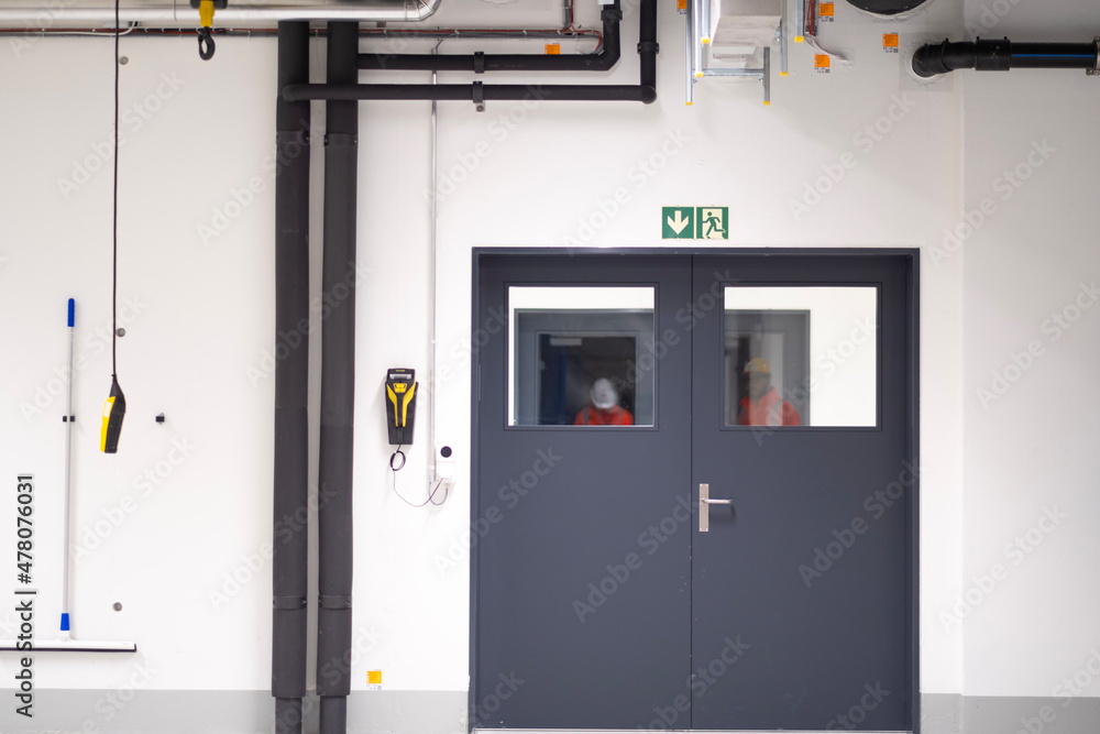 A gray industrial doorp in a modern factory hall in Zürich, surrounded by clean white walls and visible utility pipes. Ideal for themes related to industry, manufacturing, and architecture. A gray industrial doorp in a modern factory hall in Zürich, surrounded by clean white walls and visible utility pipes. Ideal for themes related to industry, manufacturing, and architecture.