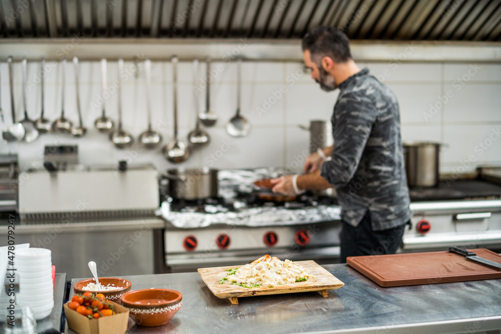 Professional cook is preparing meal in restaurant's kitchen. He is frying meat.