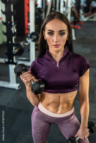  young woman trainer with beautiful press on her stomach and strong hands trains in the gym.