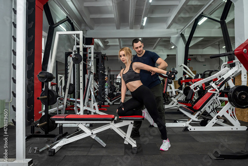 handsome trainer with muscular arms controls how the girl performs the exercises.