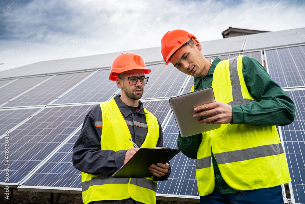 two strong skilled men in helmets and vests stand and talk in solar panels. two strong skilled men in helmets and vests stand and talk in solar panels.