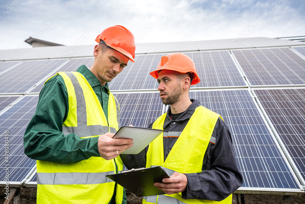 beautiful young workers in special clothes write down a plan to install solar panels. beautiful young workers in special clothes write down a plan to install solar panels.