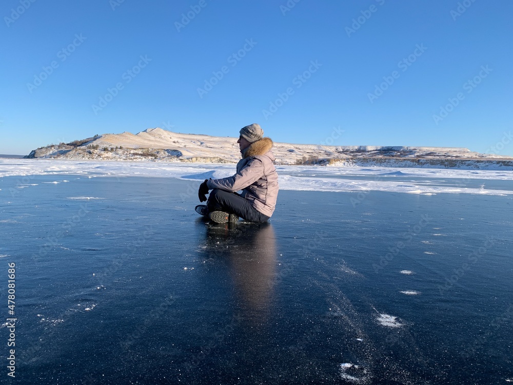 Fototapeta premium a man in winter meditates on the ice of the Volga river against the background of the hills